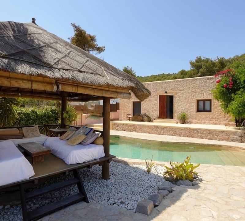 Thatched wooden gazebo with daybeds beside the pool and the stone villa building