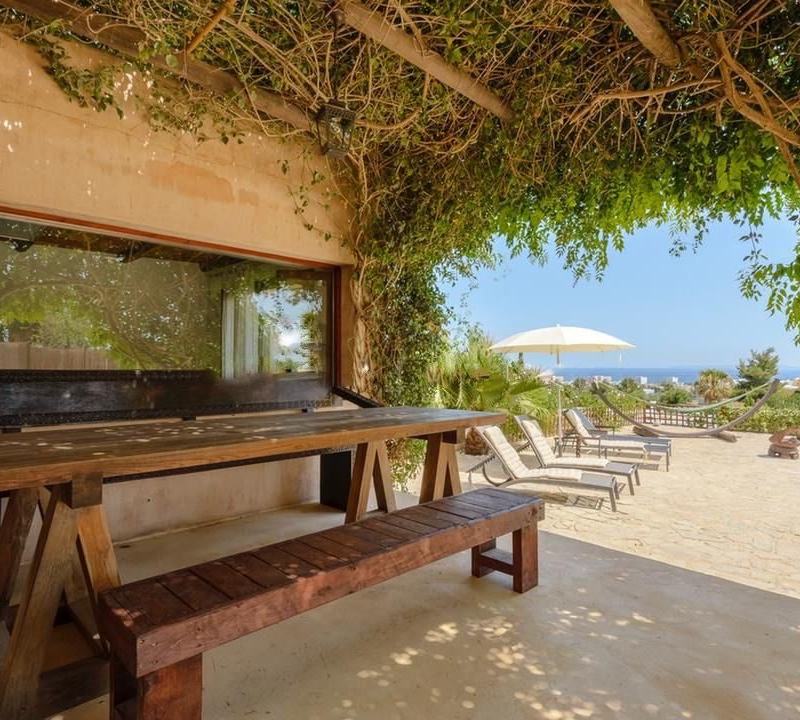 Large wooden dining table on a shaded terrace looking out towards the sea