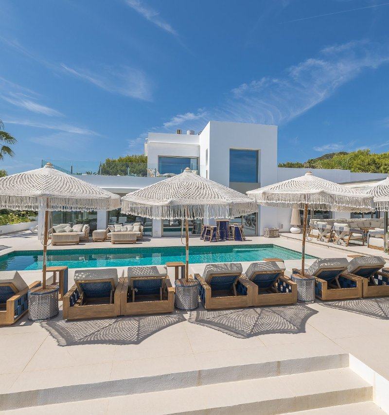 Modern white villa exterior with a swimming pool, sun terraces, and fringed umbrellas.