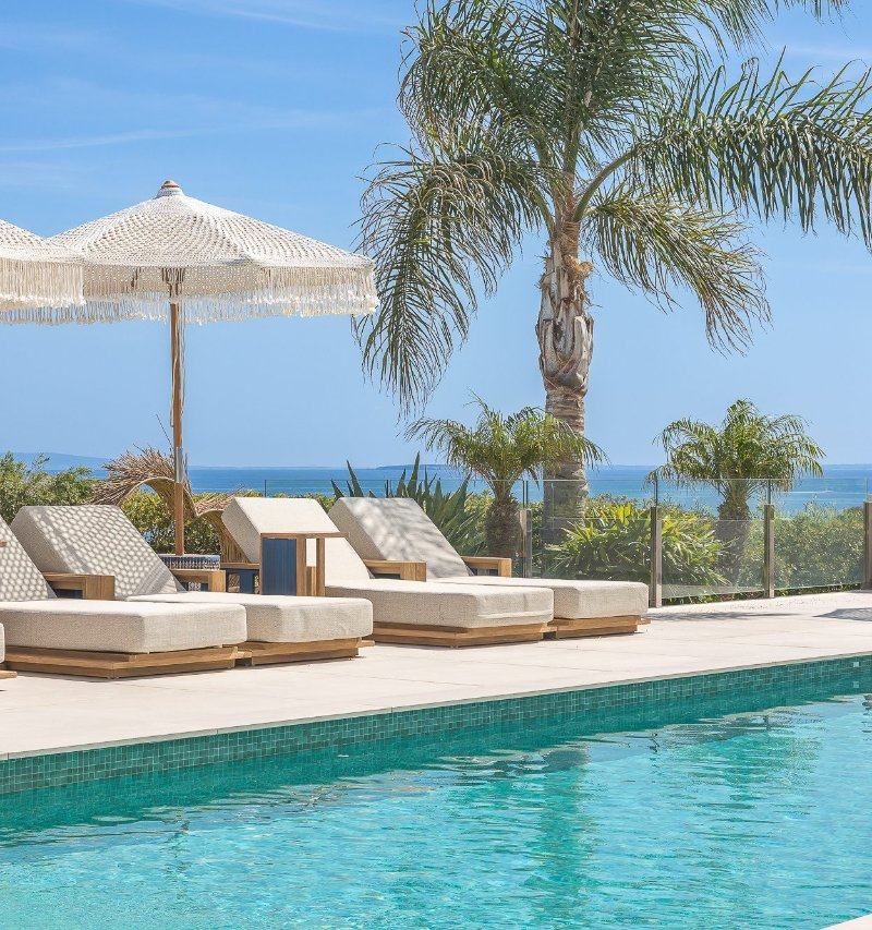 Sun loungers and a fringed umbrella beside the pool, framed by palm trees.