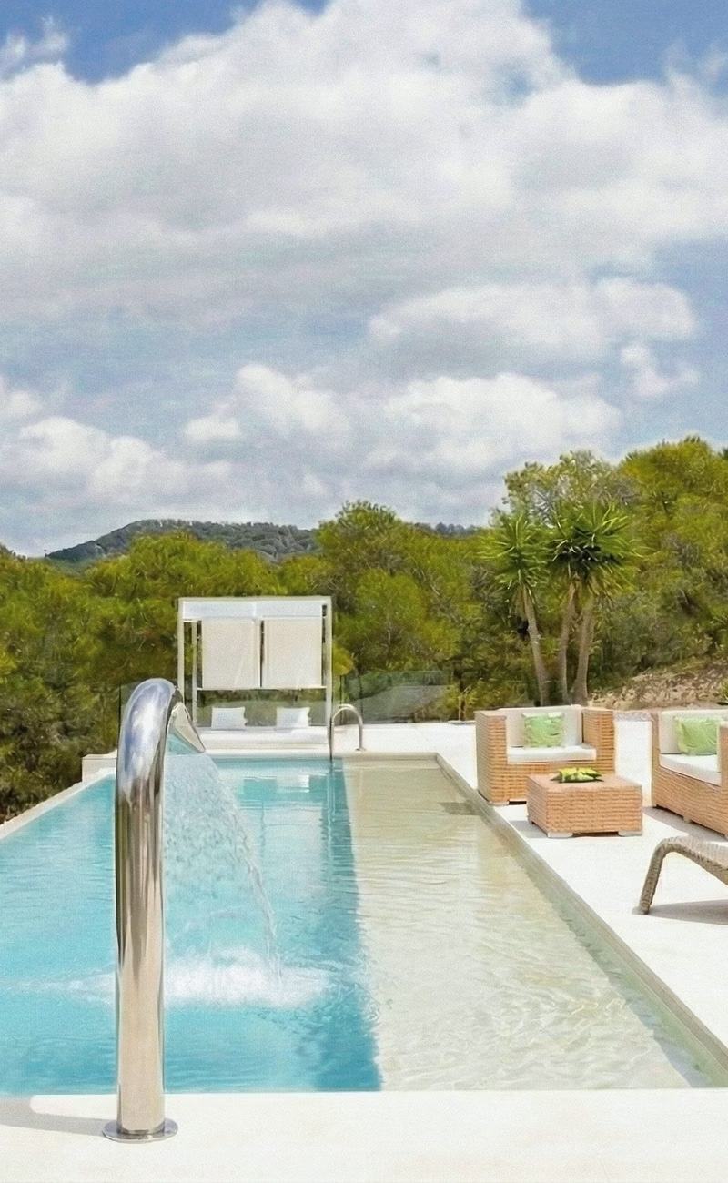 Infinity pool with a metallic waterfall, rattan armchairs, and a shaded daybed