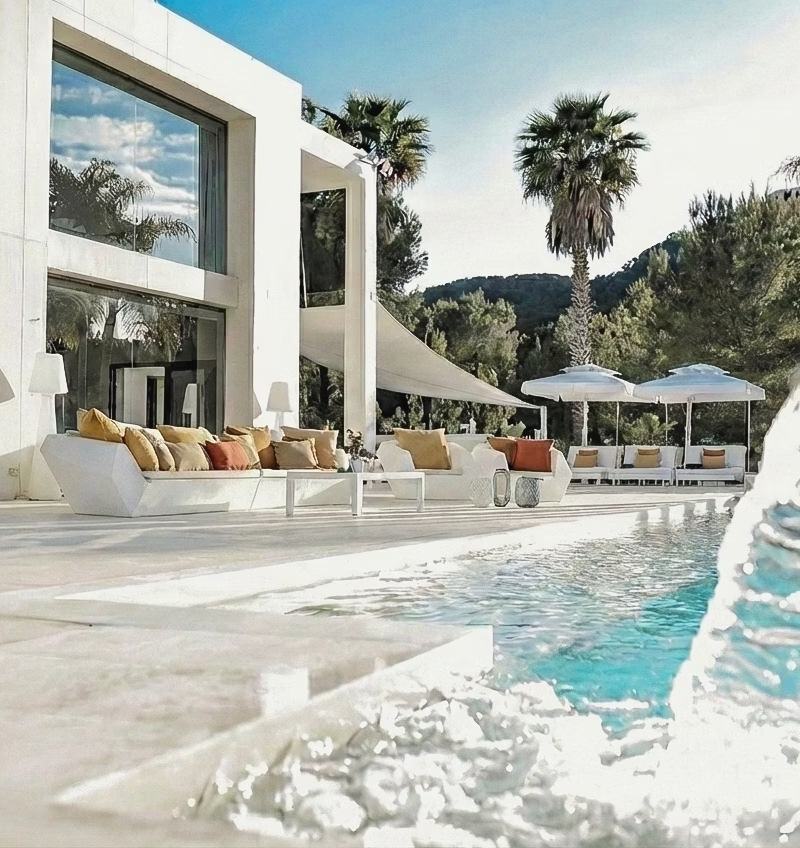 Large outdoor lounge area with white sofas, cushions, and parasols by the pool
